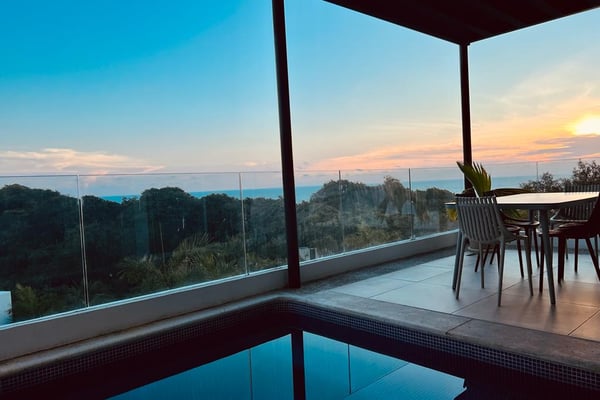 Rooftop terrace with infinity pool, dining table, and panoramic sunset view over forested landscape