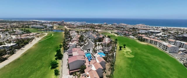 Aerial view of beachfront resort with pool, golf course, and ocean beyond